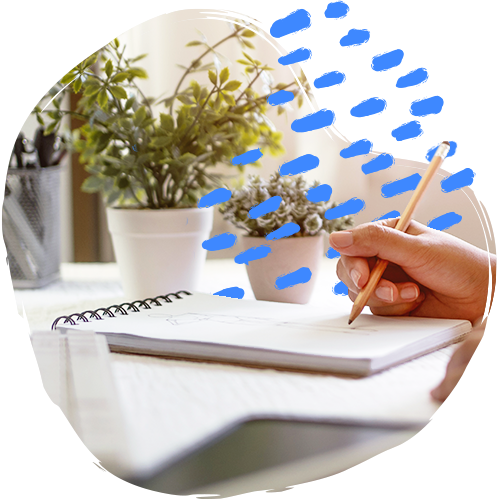 Close-up of a hand writing on a notepad with small plants in the background.